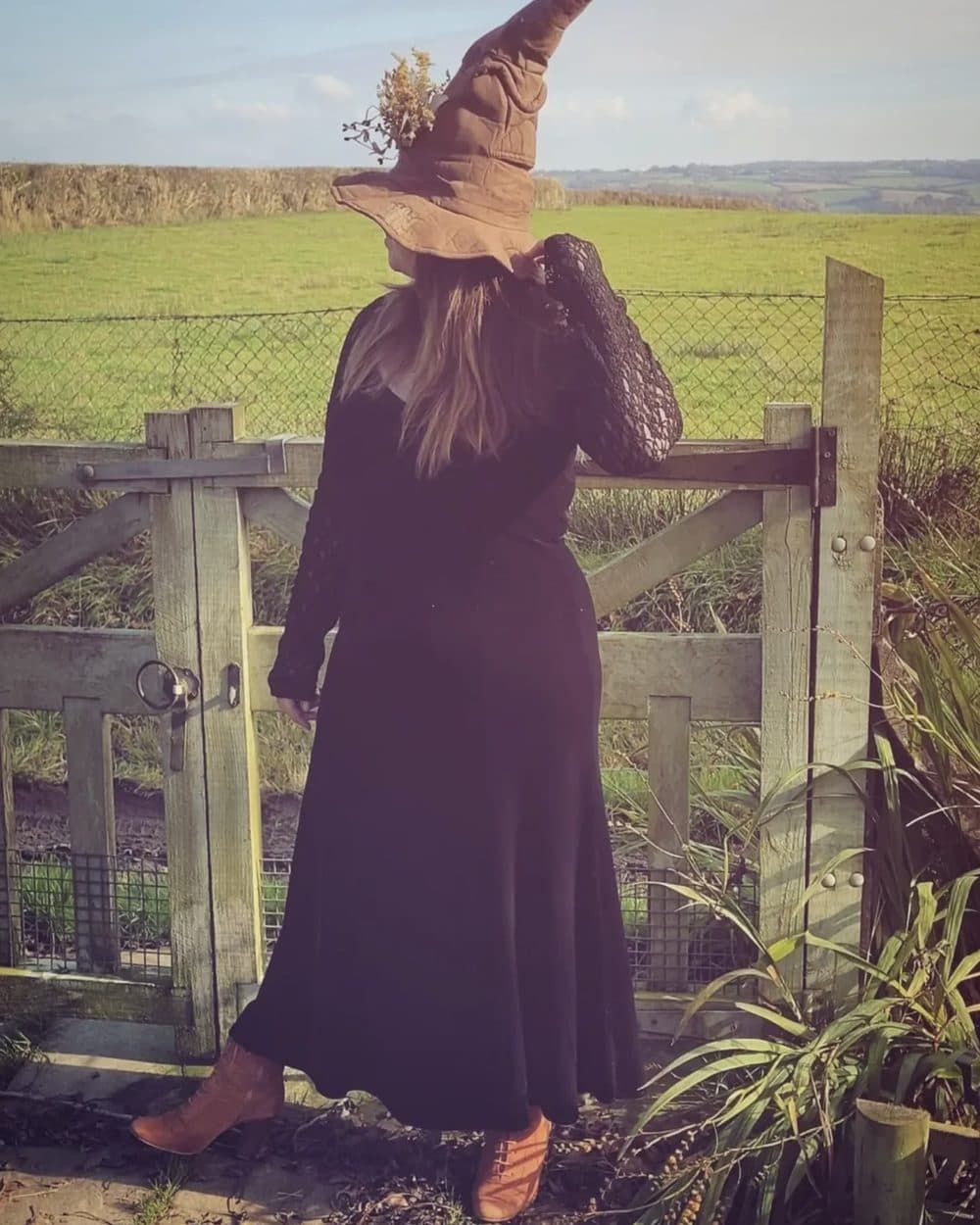 Vanessa Wiild at a Devon gate, in a tall witch's hat with dried botanicals tucked into the brim